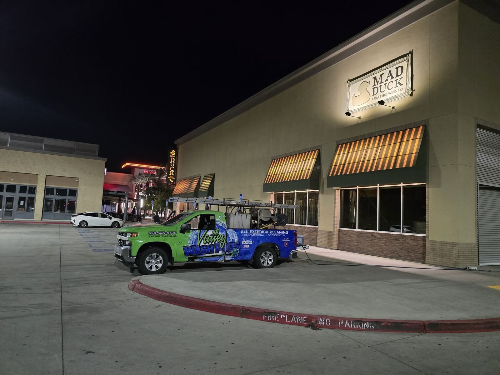 Valley Wash Pros truck pressure washing a shopping center storefront and parking lot at night