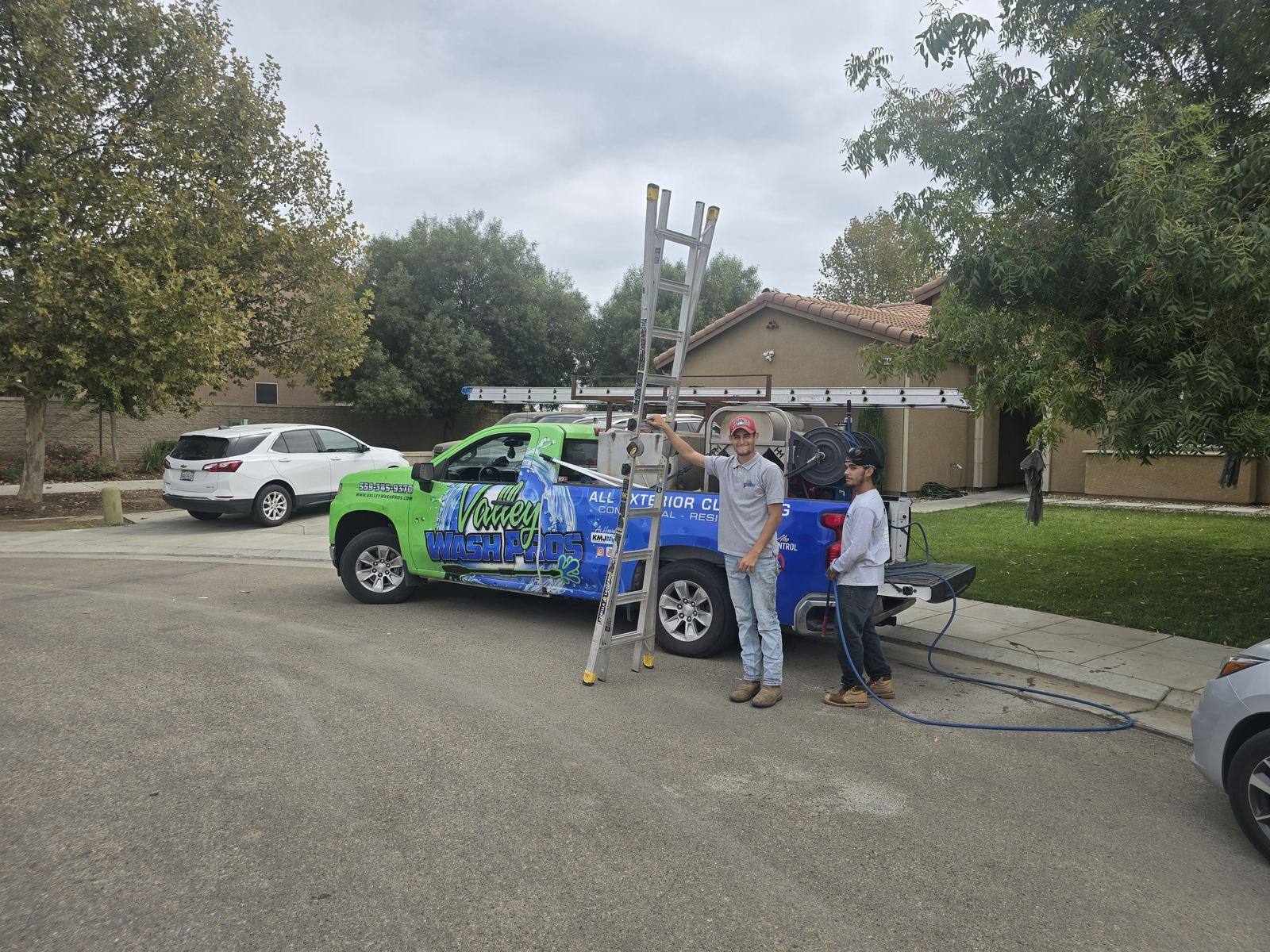 Technician carrying an extension ladder next to a Valley Wash Pros service truck