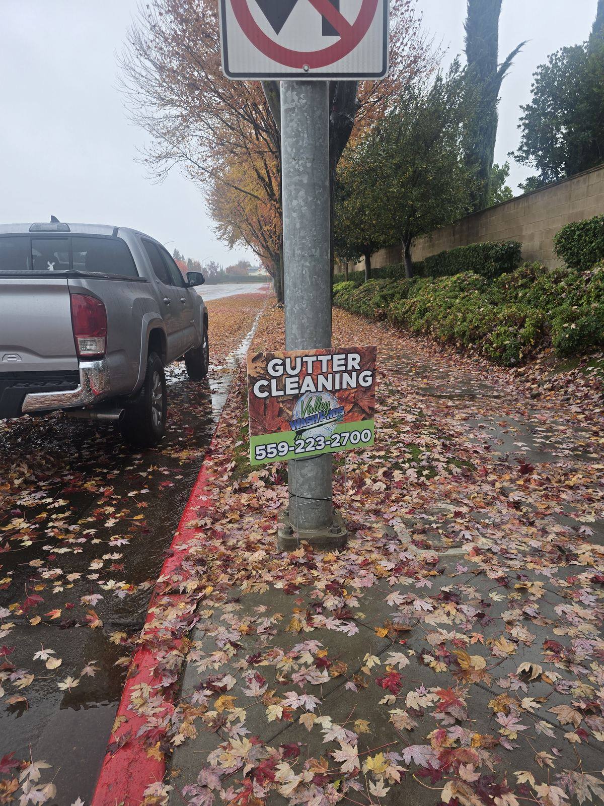Valley Wash Pros gutter cleaning yard sign on a Fresno curb buried in wet fall leaves