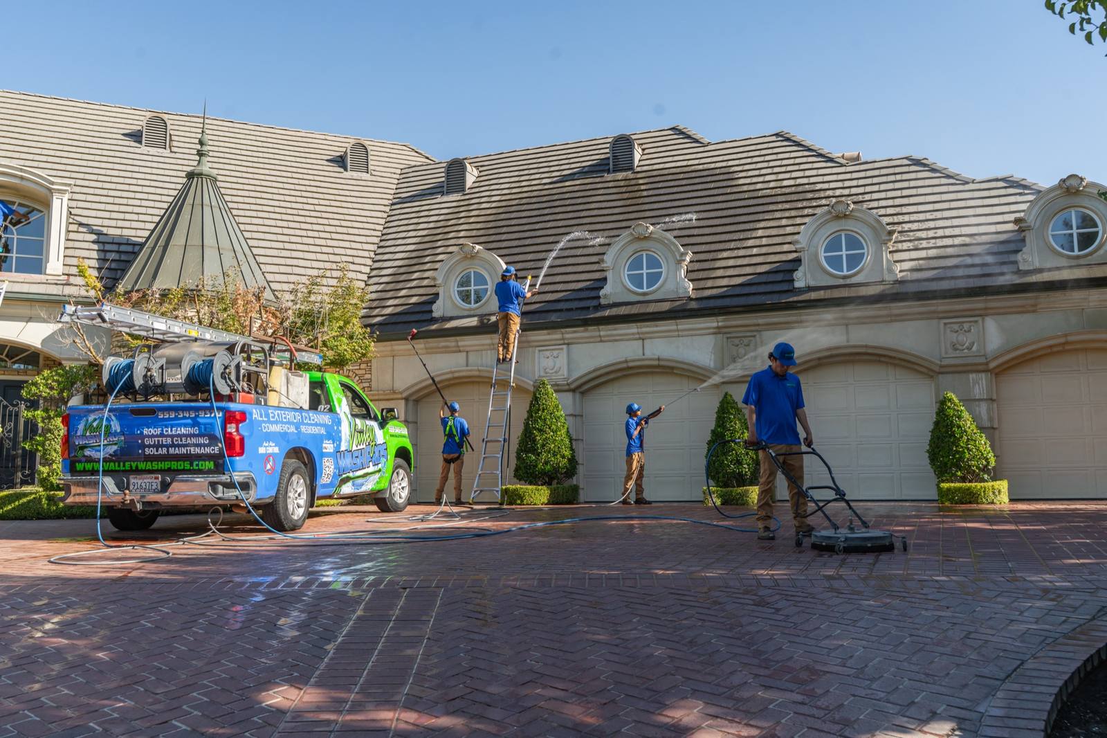 Valley Wash Pros crew working the roofline, garage bays and driveway of a large Fresno home