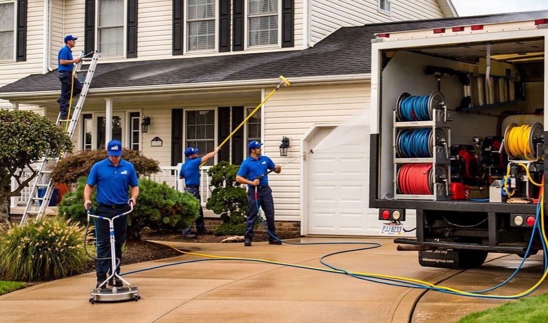 Technician on a ladder soft washing the eaves and roofline of a home